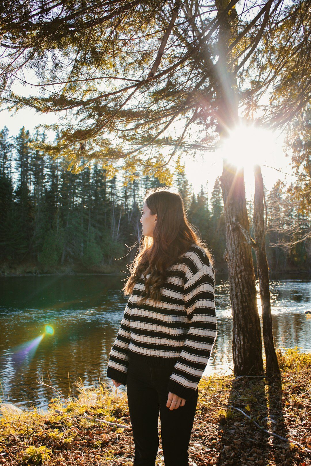 Woman standing in a sunlit forest wearing a wool sweater